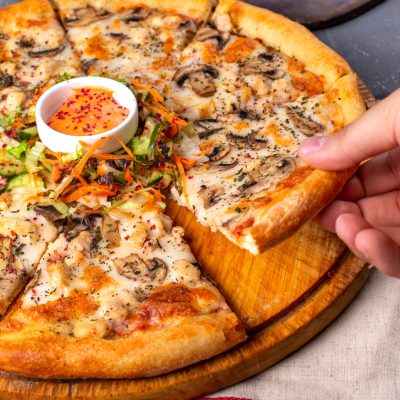 side view of pizza with chicken and mushrooms served with sauce and vegetables salad on a wooden plate